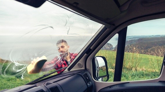 Utsikt från insidan husbil av man i rutig röd skjorta som rengör vindruta med svamp.